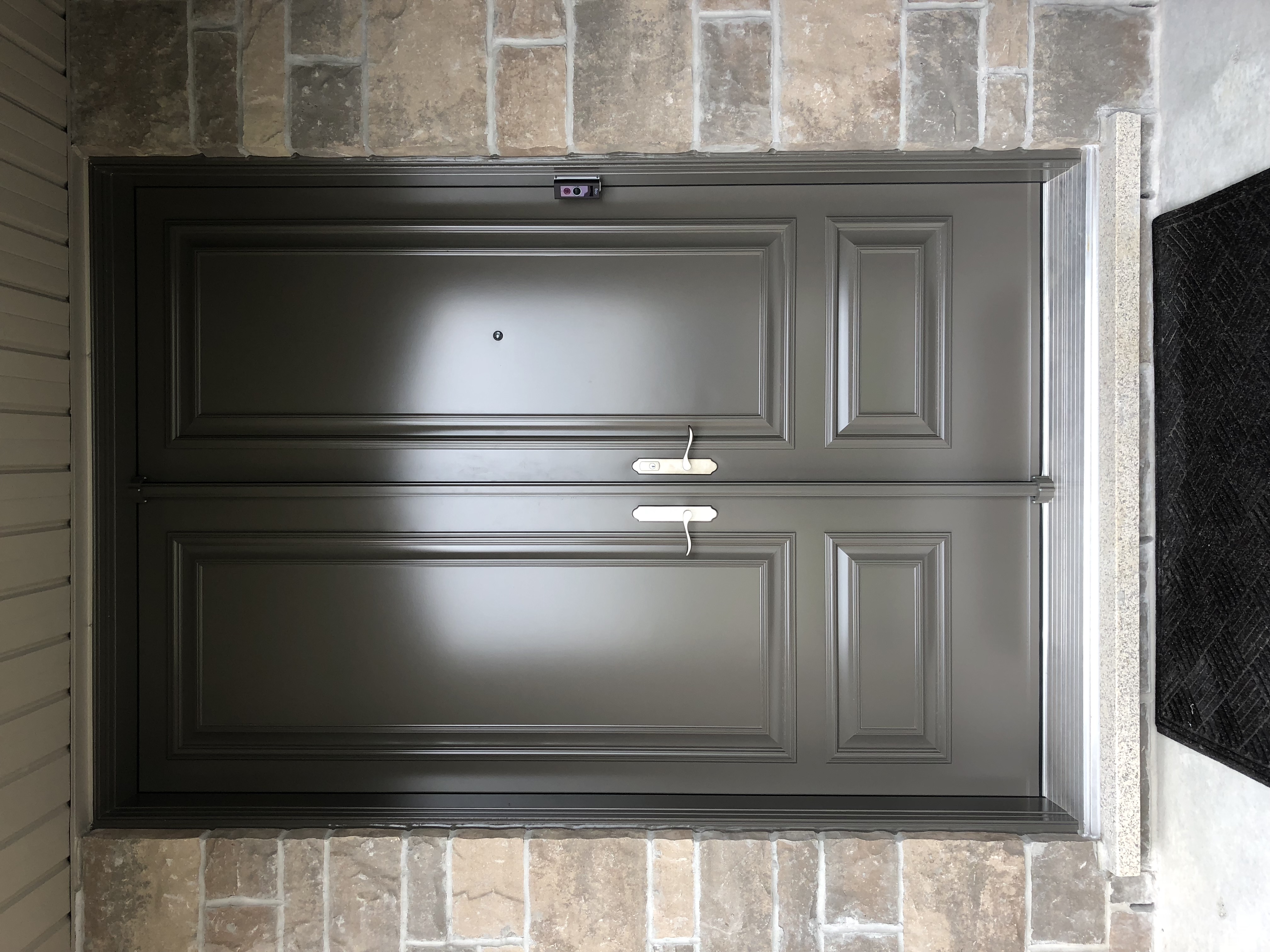 Modern double front entrance door with a smooth grey finish, raised panel design, silver hardware, and stone masonry framing on a Toronto home.