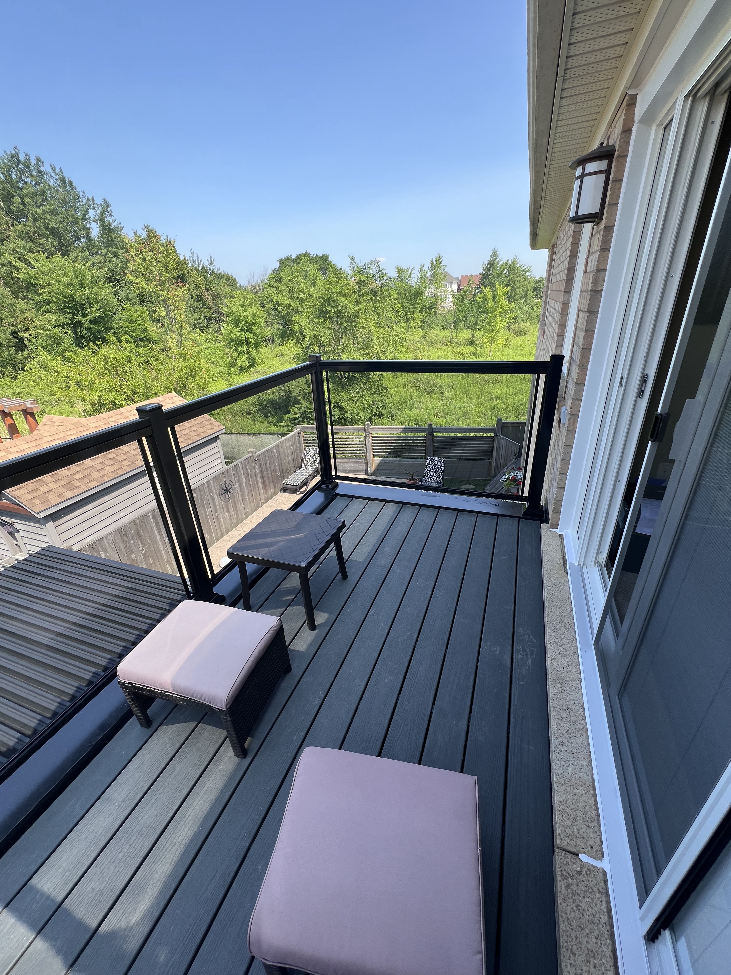 Toronto balcony with new black metal and glass railings, composite decking, and outdoor seating overlooking a landscaped yard.