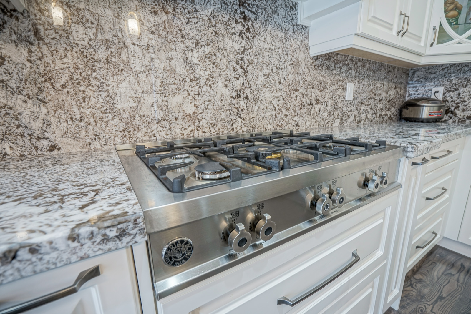 Gas stove integration in custom kitchen made of white cabinetry, marble backsplash. 