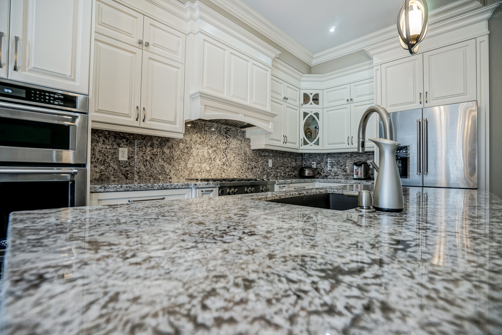 Modern kitchen with white cabinetry, marble backsplash, stainless steel gas range with pot filler, fluted upper cabinets, and open shelves displaying decorative items under warm accent lighting.