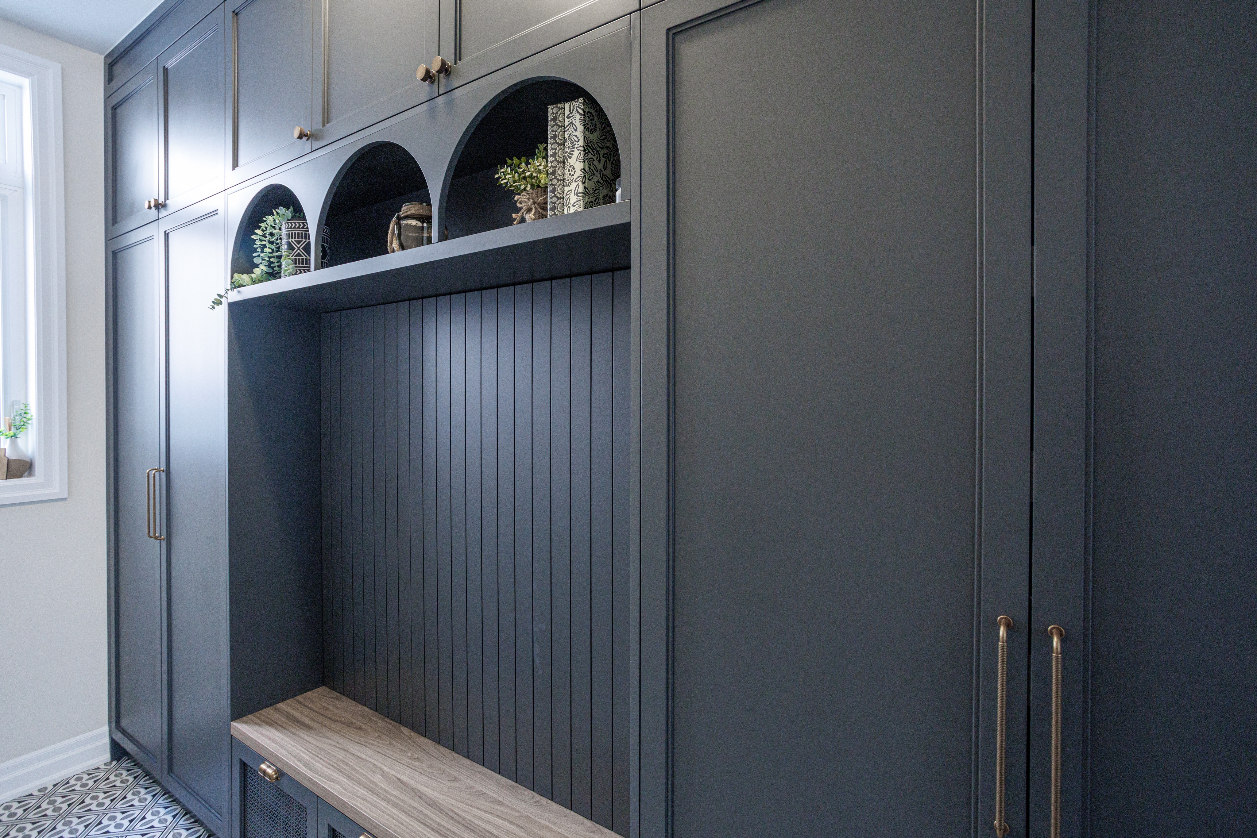 Custom built‑in cabinetry with matte dark grey doors, brass handles, arched cubbies, and a wood bench in a North York / Toronto home.