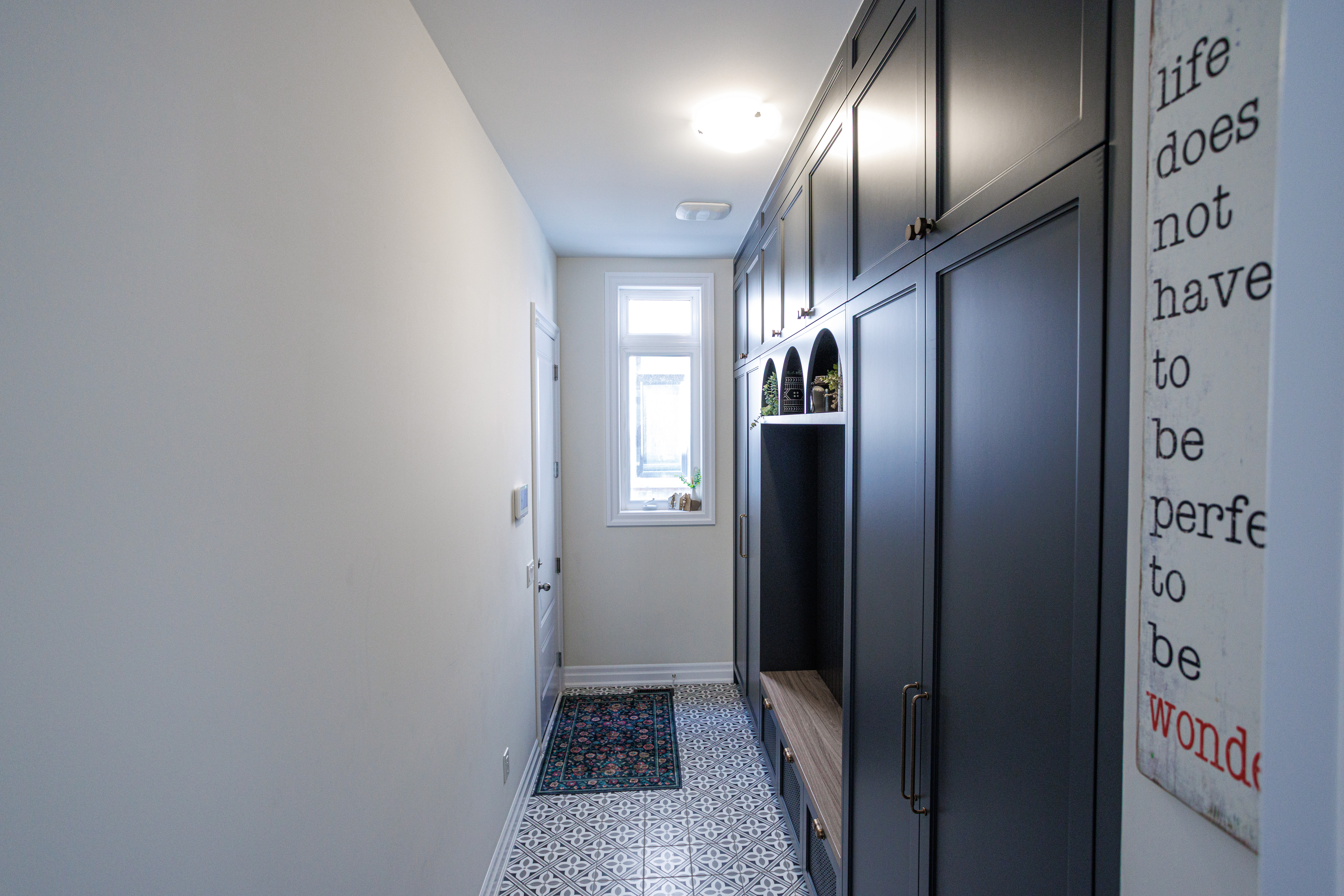Custom built‑in cabinetry with matte dark grey doors, brass handles, arched cubbies, and a wood bench in a North York / Toronto home.