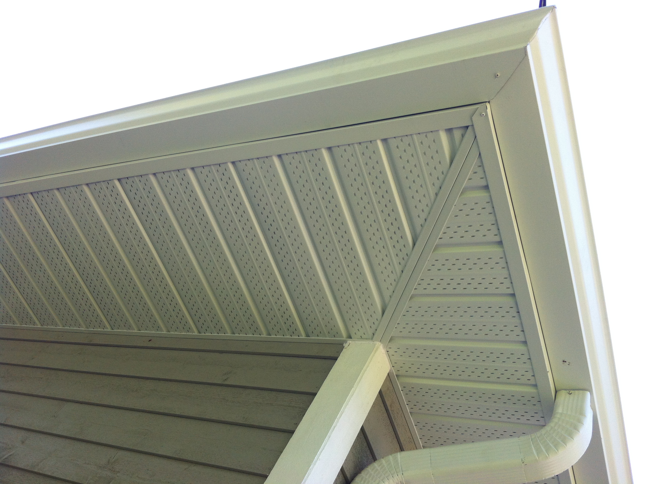Close‑up of newly installed vented soffit panels, clean fascia trim, seamless eavestrough, and a matching downspout on a Mississauga home, with siding visible below the roofline.